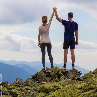 Ein Paar steht mit erhobenen Händen auf dem Berggipfel